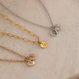 Three custom initial charm necklaces in gold, silver, and rose gold finishes, each with distinct chain styles and personalized round charms on a marble surface.