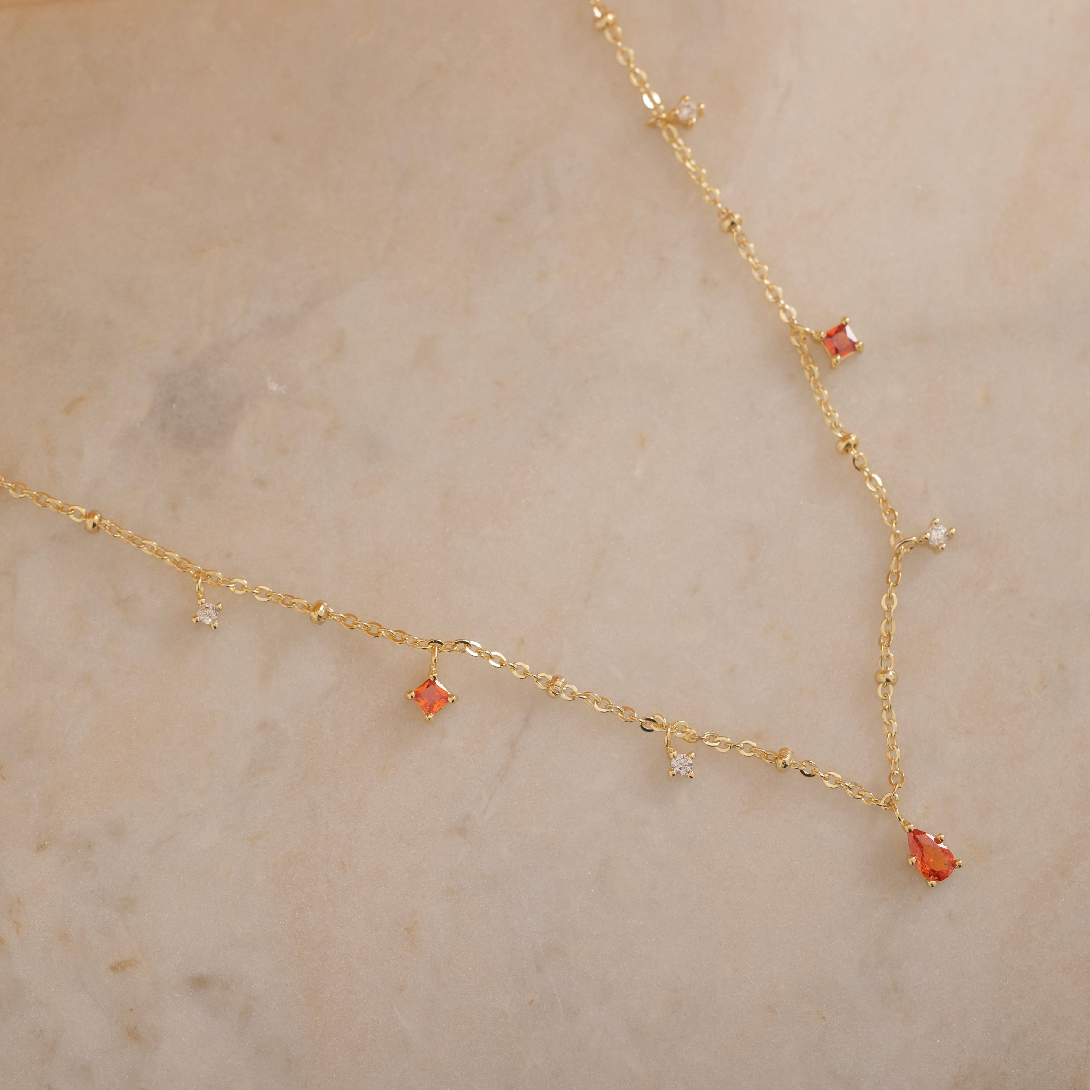 
Dainty sterling silver and 14k gold plated necklace featuring four square orange-colored cubic zirconia stones, one centered teardrop-shaped orange stone, and four white cubic zirconia accents between the orange birthstones. 