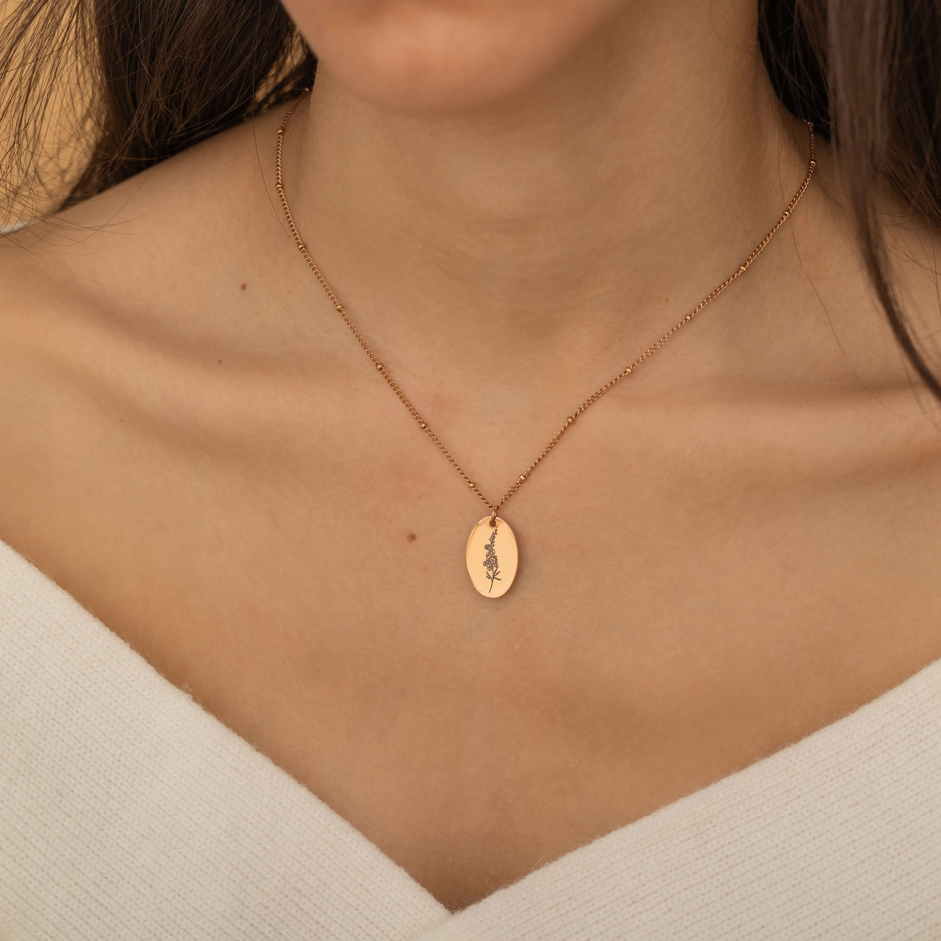 Up-close view of a rose gold personalized birth flower necklace engraved, worn by a woman.