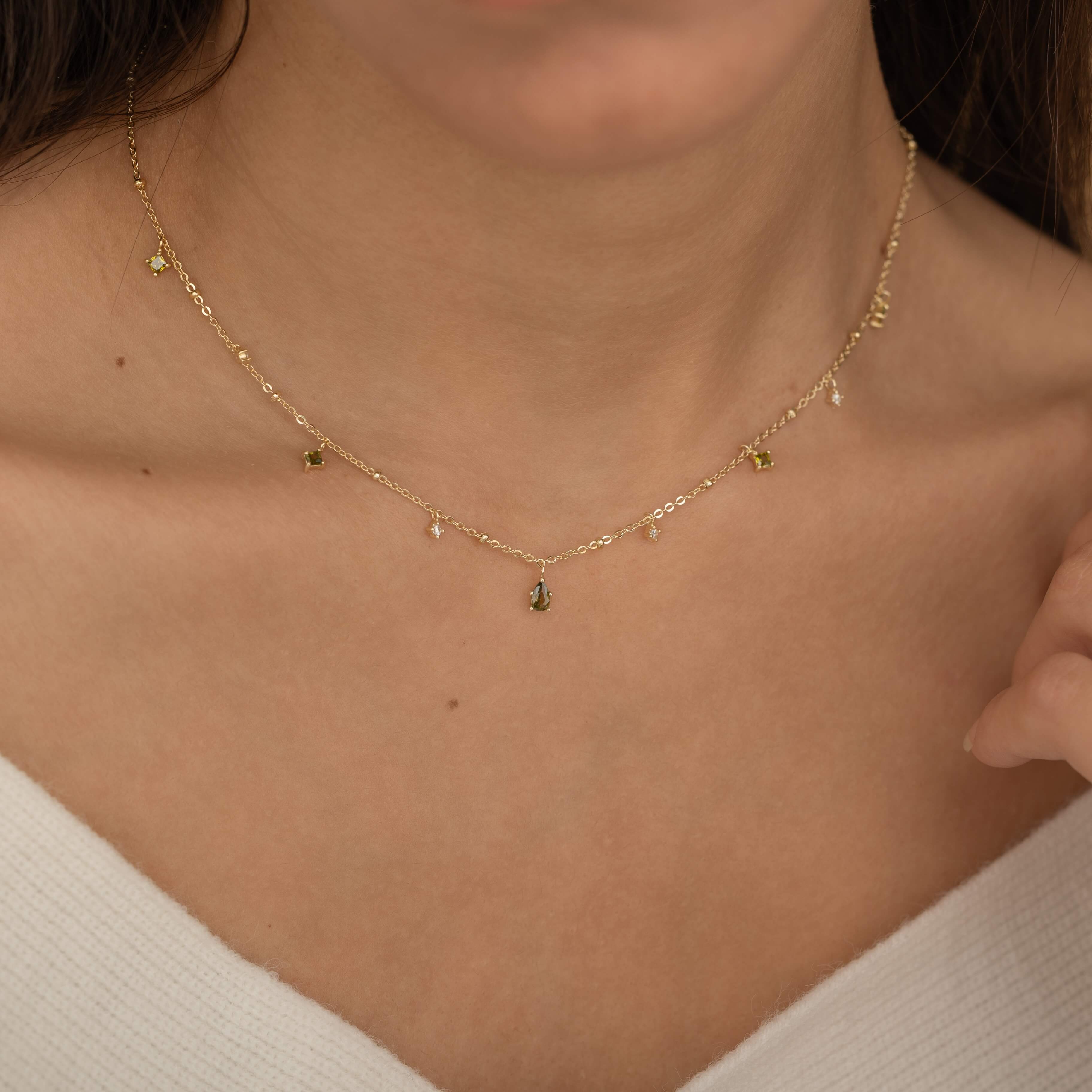 Dainty sterling silver and 14k gold plated necklace featuring four square peridot-colored cubic zirconia stones, one centered teardrop-shaped peridot stone, and four white cubic zirconia accents between the peridot.
