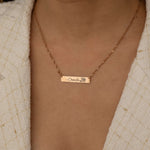 Close-up of a rose gold bar necklace with a personalized birth flower design and a name engraved as the flower's stem, worn by a woman.