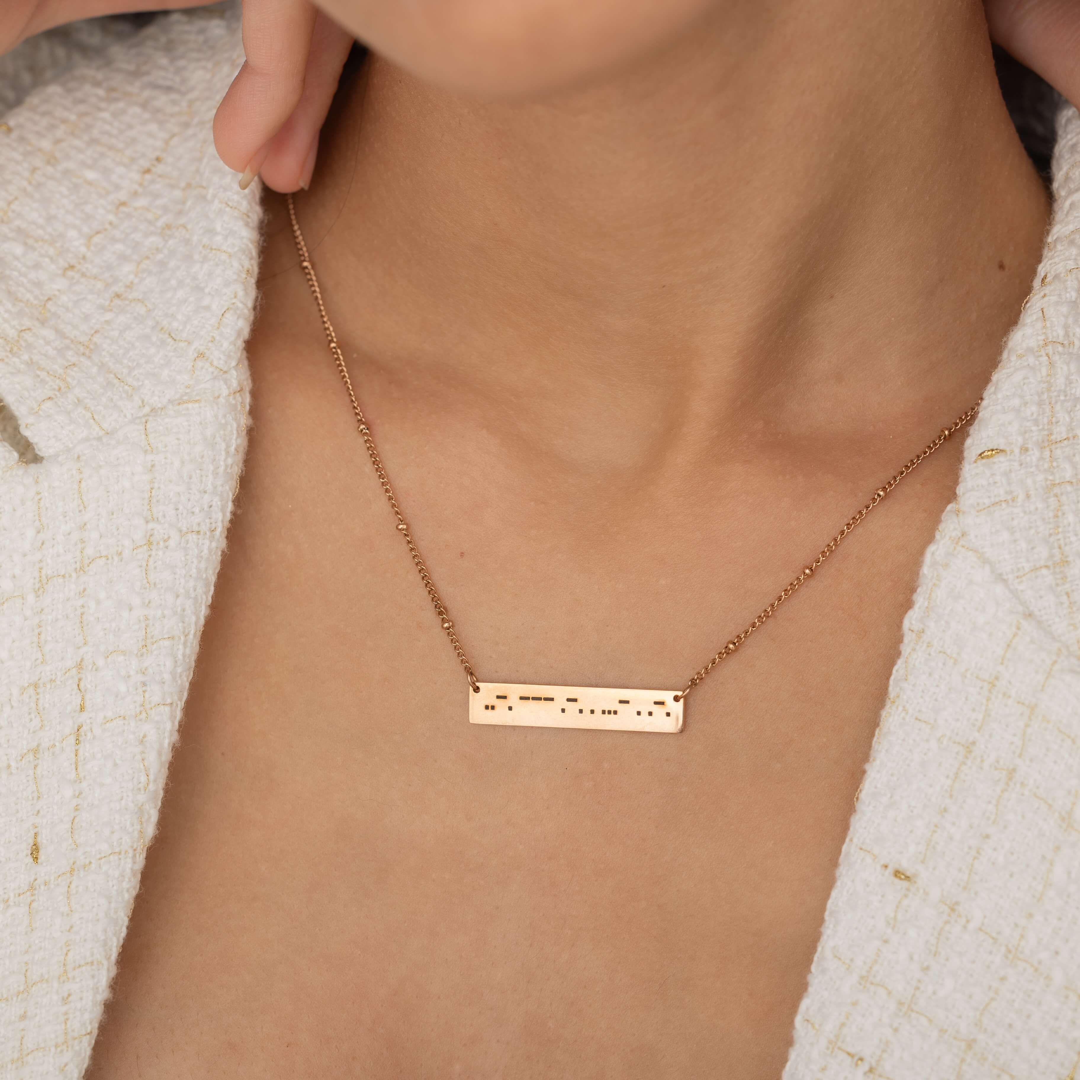Close-up of a rose gold bar necklace engraved with a personalized Morse code message, worn by a woman.