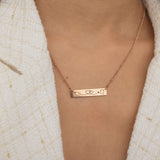 Close-up of a rose gold bar necklace engraved with two state outlines at each corner and a heart in the middle connecting them, worn by a woman.
