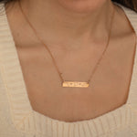 Close-up of a rose gold bar necklace engraved with three state outlines and two connecting hearts between them, worn by a woman.