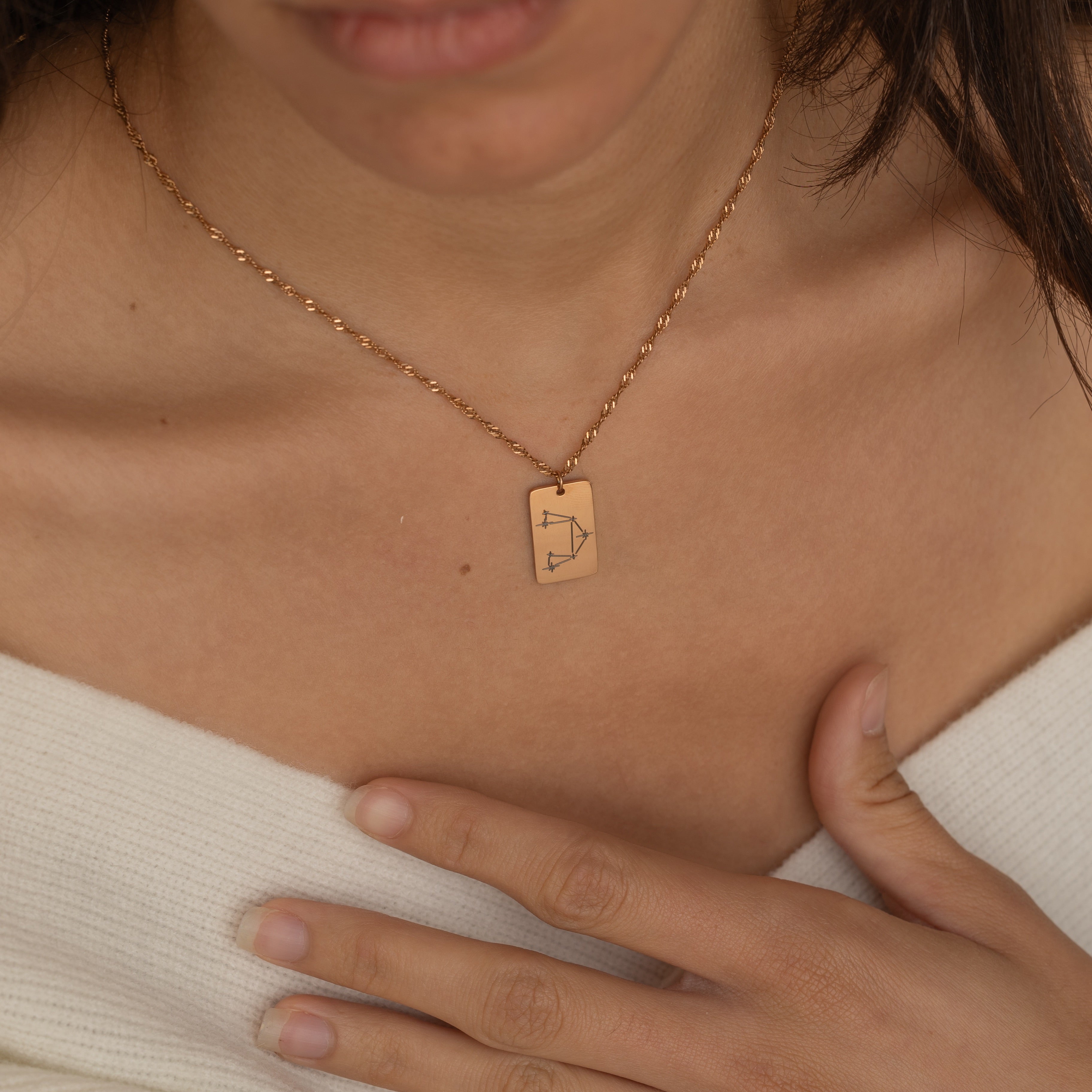 Close-up of a constellation necklace pendant worn by a woman, showcasing a minimalist engraved star pattern.