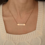 Close-up of a rose gold pendant necklace engraved with coordinates worn by a woman.