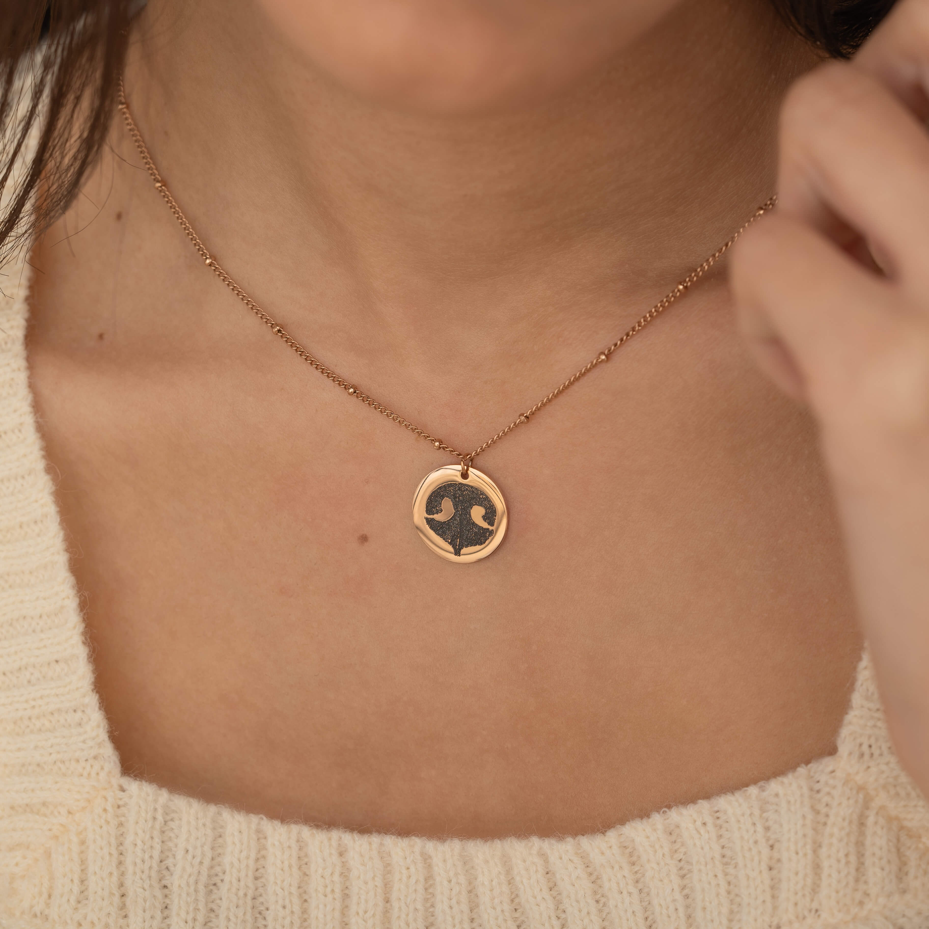 Close-up of a rose gold pendant necklace featuring an engraved dog nose print design worn by a woman.