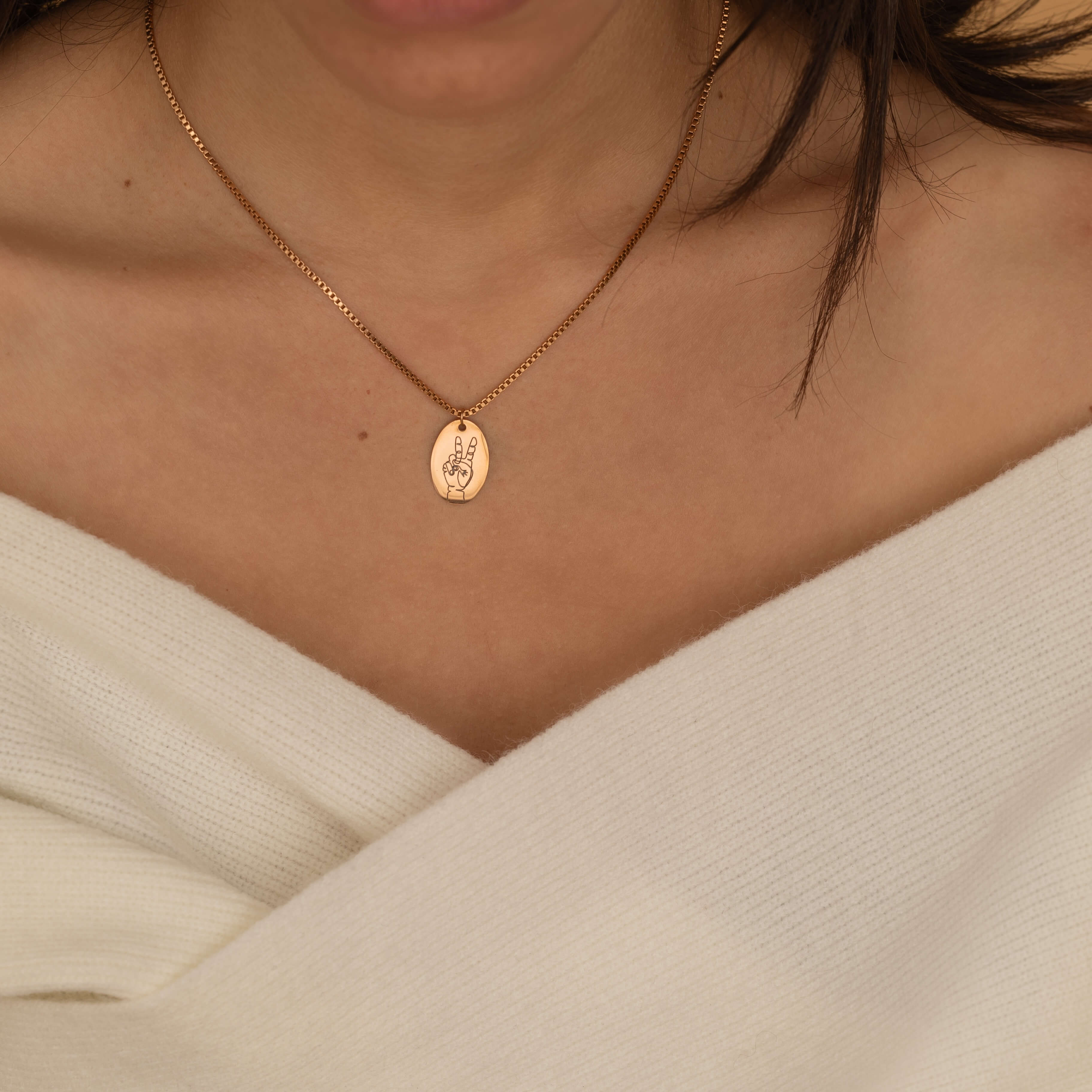 close up of a rose gold hand gesture necklace worn by a women showcasing a peace sign.
