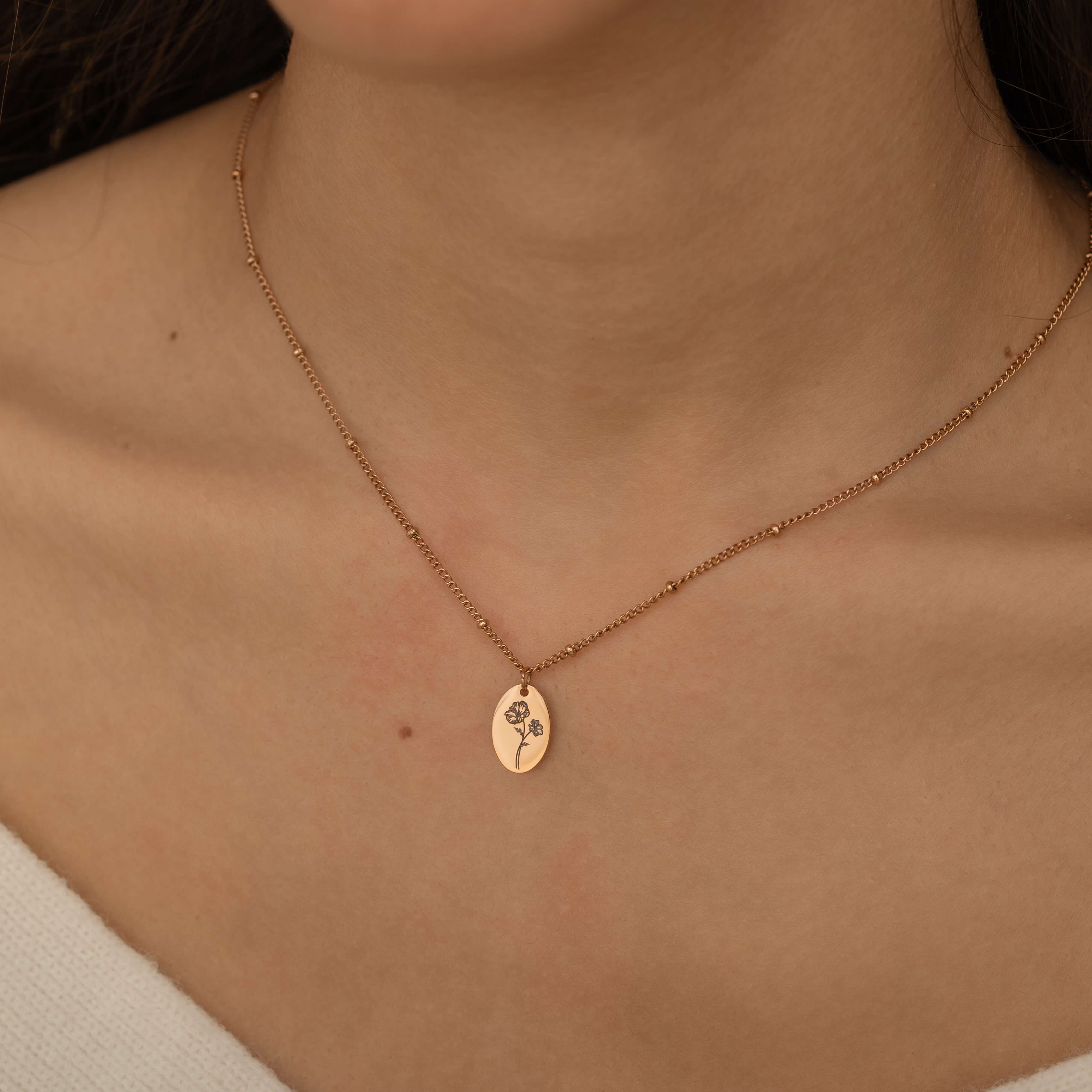 Close-up of a rose gold necklace engraved with a birth flower representing family member, worn by a woman.