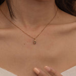 Close-up of a rose gold necklace with engraved pendant, featuring an initial, worn by a woman.