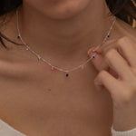 Dainty sterling silver necklace featuring four square sapphire-colored cubic zirconia stones, one centered teardrop-shaped sapphire stone, and four white cubic zirconia accents between the sapphire.