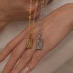 Gold and silver rectangular pendants with tiger engravings, featuring a sparkling cubic zirconia accent. They symbolize the strength tarot necklace. Available in both gold-plated and sterling silver chains.