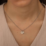 Close-up of a silver custom birth flower engraved pendant necklace worn by a woman, showcasing two round charms with floral engravings.