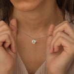 Close-up of a silver custom birth flower engraved pendant necklace worn by a woman, showcasing two round charms with floral engravings being held between fingers.
