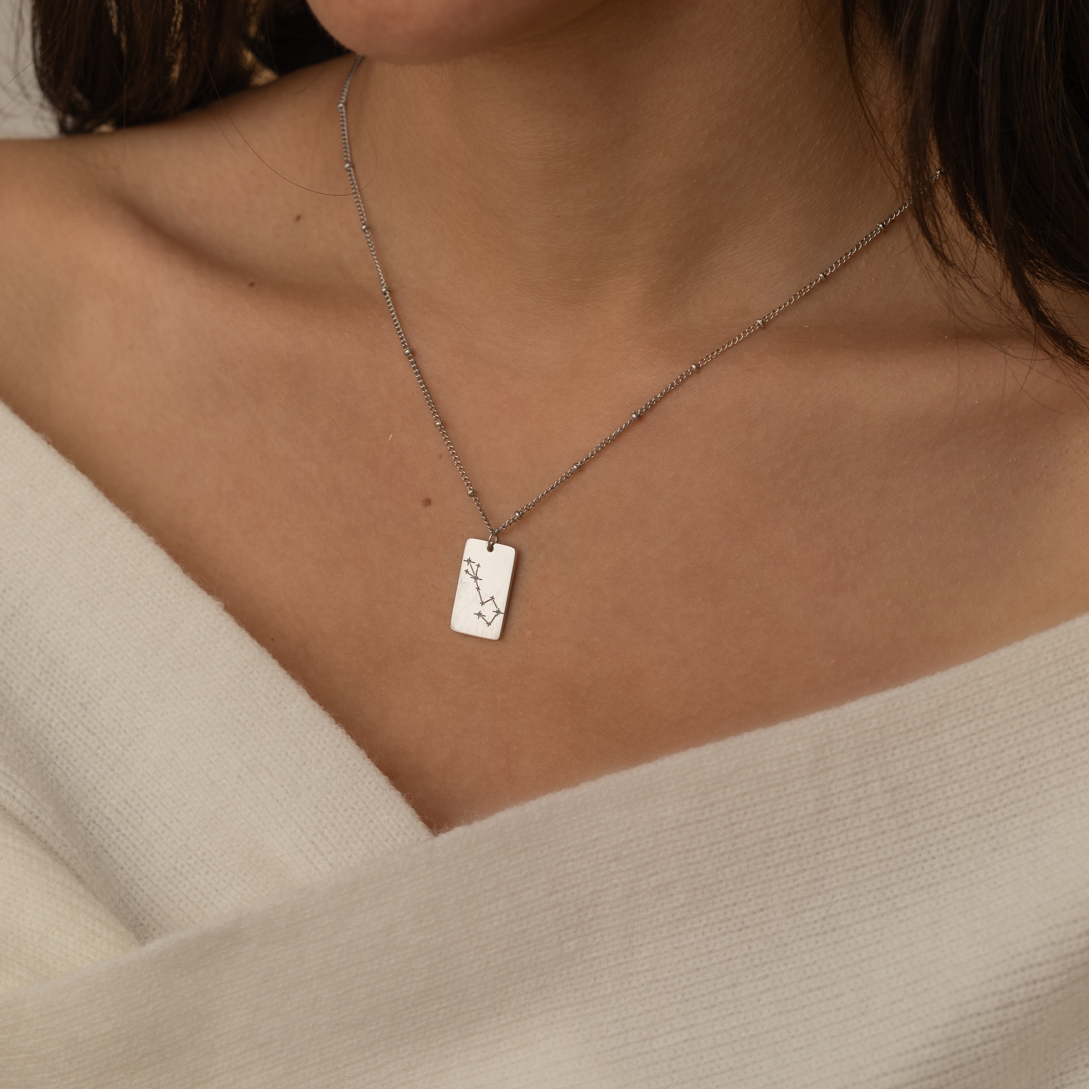 Close-up of a constellation necklace pendant worn by a woman, showcasing a minimalist engraved star pattern.