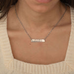 Close-up of a silver pendant necklace engraved with coordinates worn by a woman.