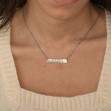 Close-up of a silver pendant necklace engraved with coordinates worn by a woman.