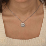 Silver pendant necklace featuring an engraved outline of dog ears with a pet's name underneath, worn by a woman.