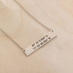 Close-up of a silver pendant necklace engraved with coordinates worn by a woman.