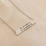 Close-up of a silver pendant necklace engraved with coordinates worn by a woman.