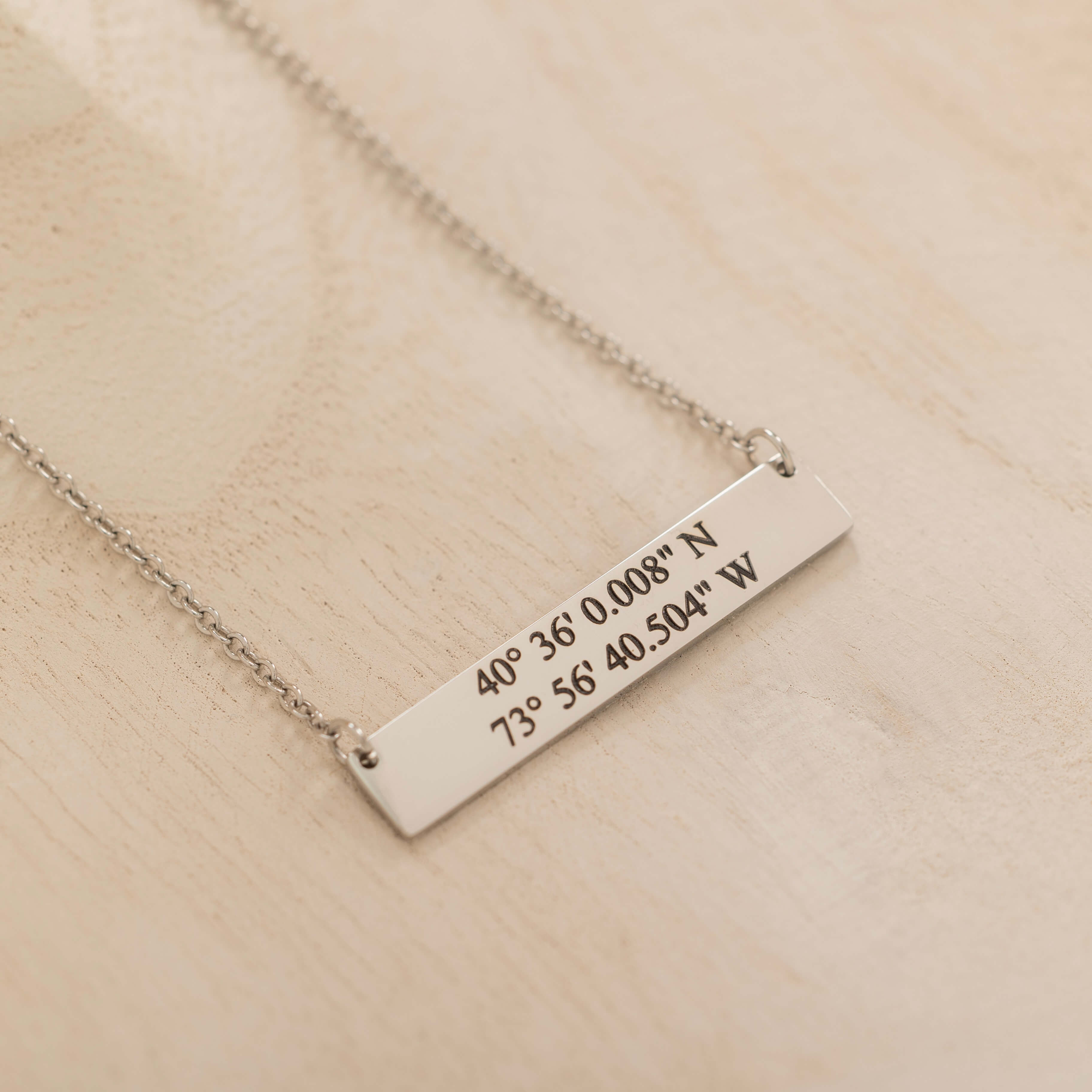 Close-up of a silver pendant necklace engraved with coordinates worn by a woman.