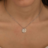 Close-up of a silver necklace with multiple pendants, each engraved with a birth flower representing different family members, worn by a woman.