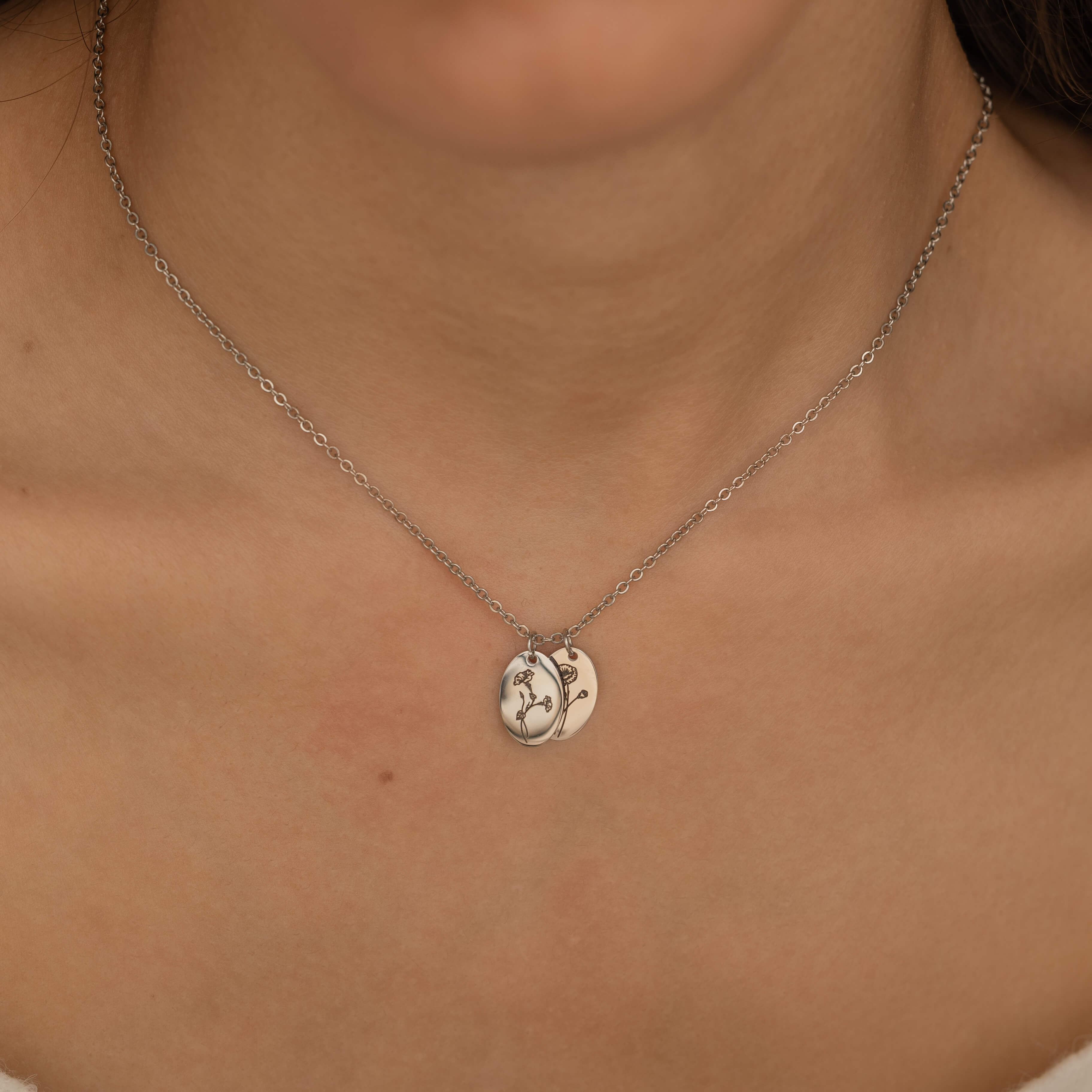 Close-up of a silver necklace with multiple pendants, each engraved with a birth flower representing different family members, worn by a woman.