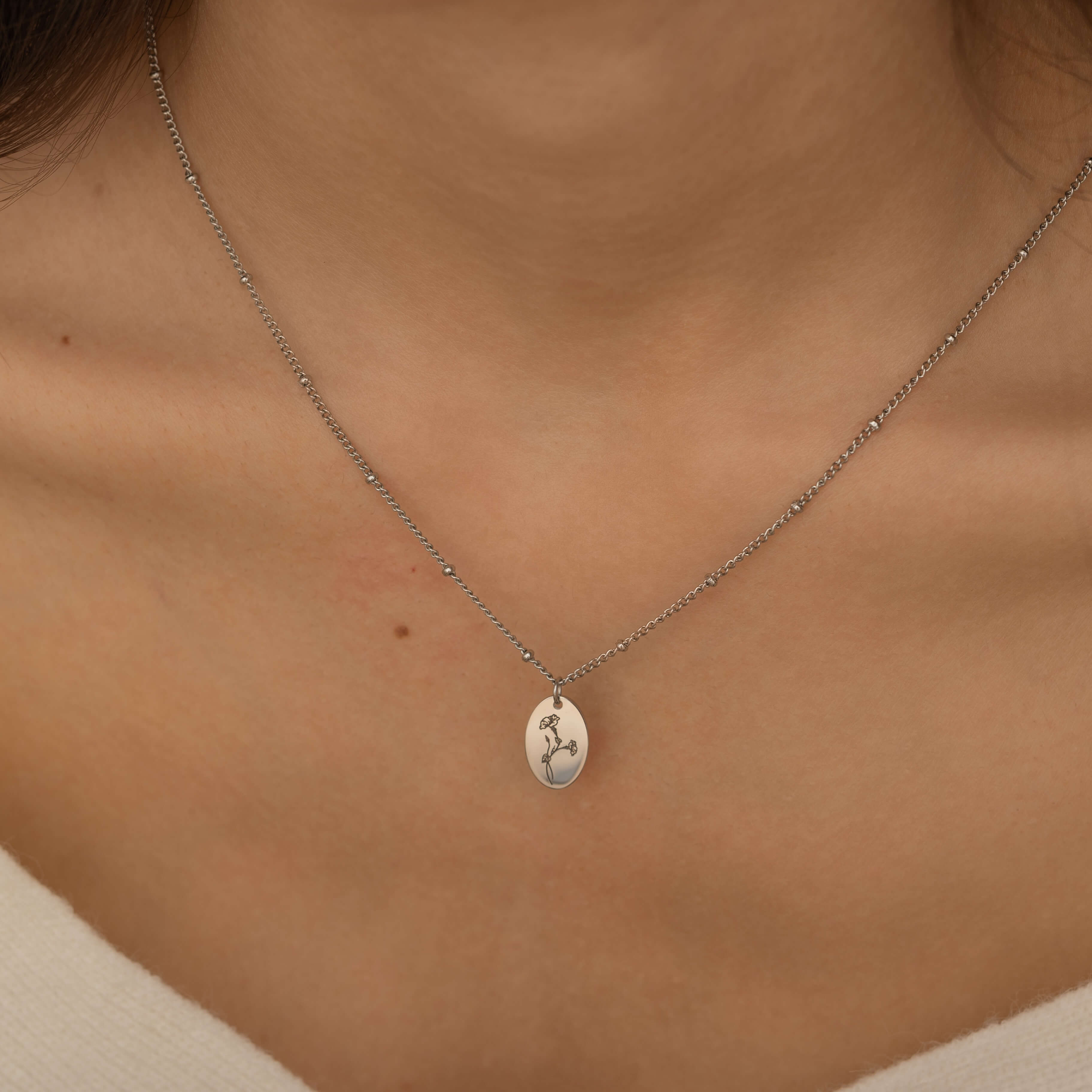 Close-up of a silver necklace engraved with a birth flower representing family member, worn by a woman.