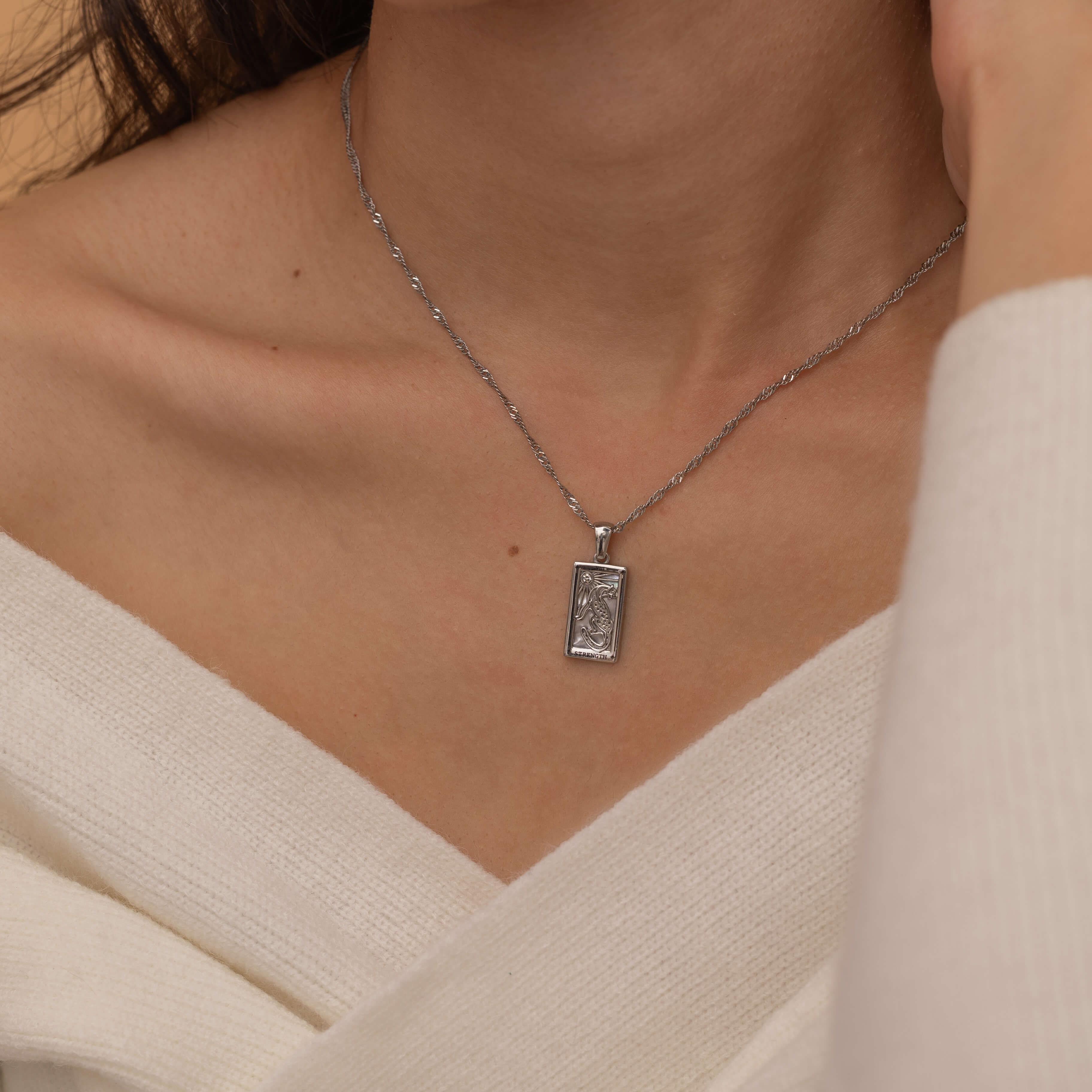 Gold and silver rectangular pendants with tiger engravings, featuring a sparkling cubic zirconia accent. They symbolize the strength tarot necklace. Available in both gold-plated and sterling silver chains.