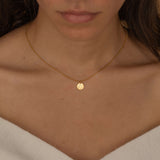 Close-up of a gold pendant necklace featuring an engraved outline of the state of Texas worn by a woman.