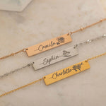 Close-up of three gold bar necklace with a personalized birth flower design each and names engraved as the flower's stem.