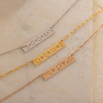 Close-up of three bar necklaces each engraved with three state outlines and two connecting hearts between them, on top of a stone.