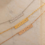 Close-up of three bar necklaces each engraved with three state outlines and two connecting hearts between them, on top of a stone.