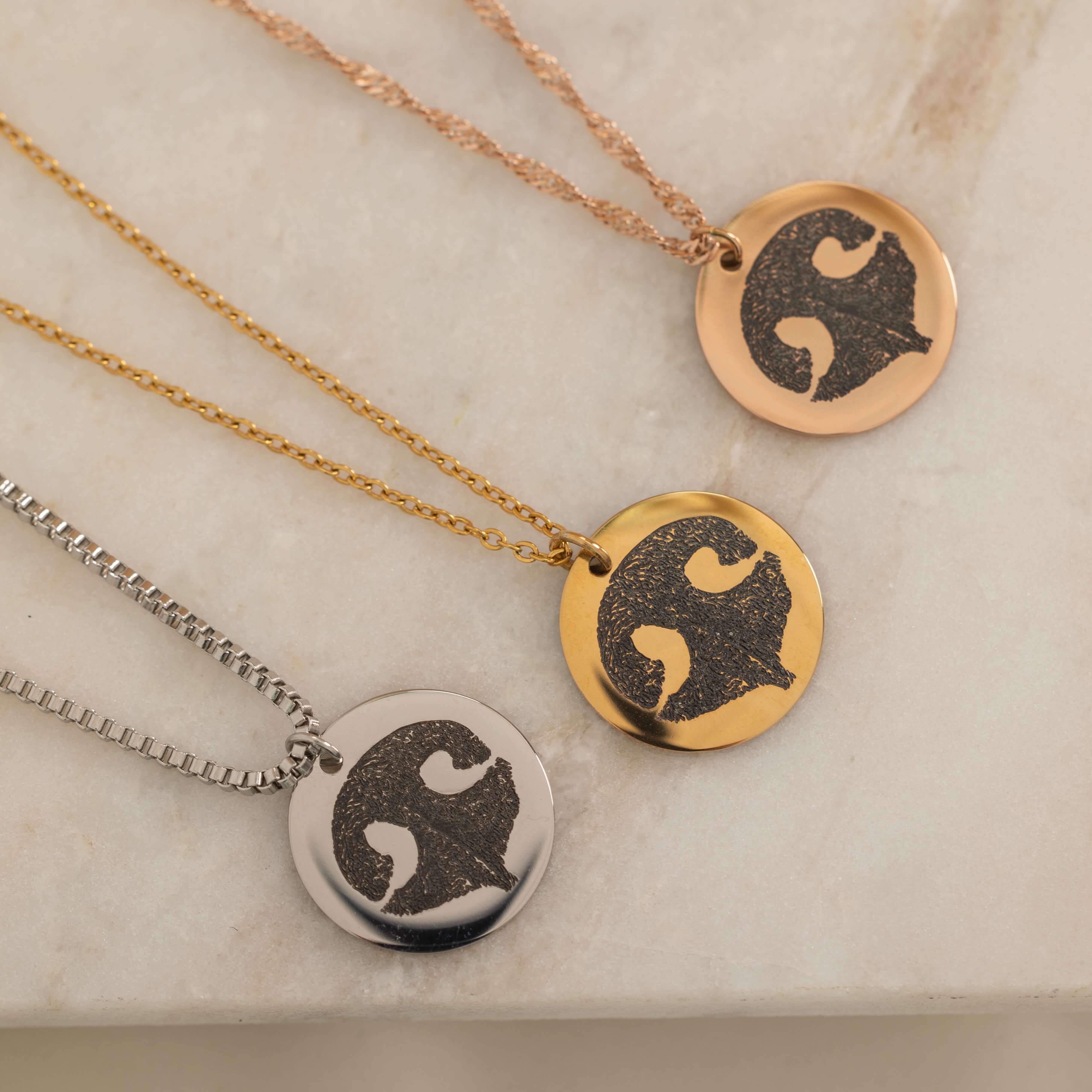 Close-up of three pendant necklace featuring engraved dog nose print designs on top of a stone.