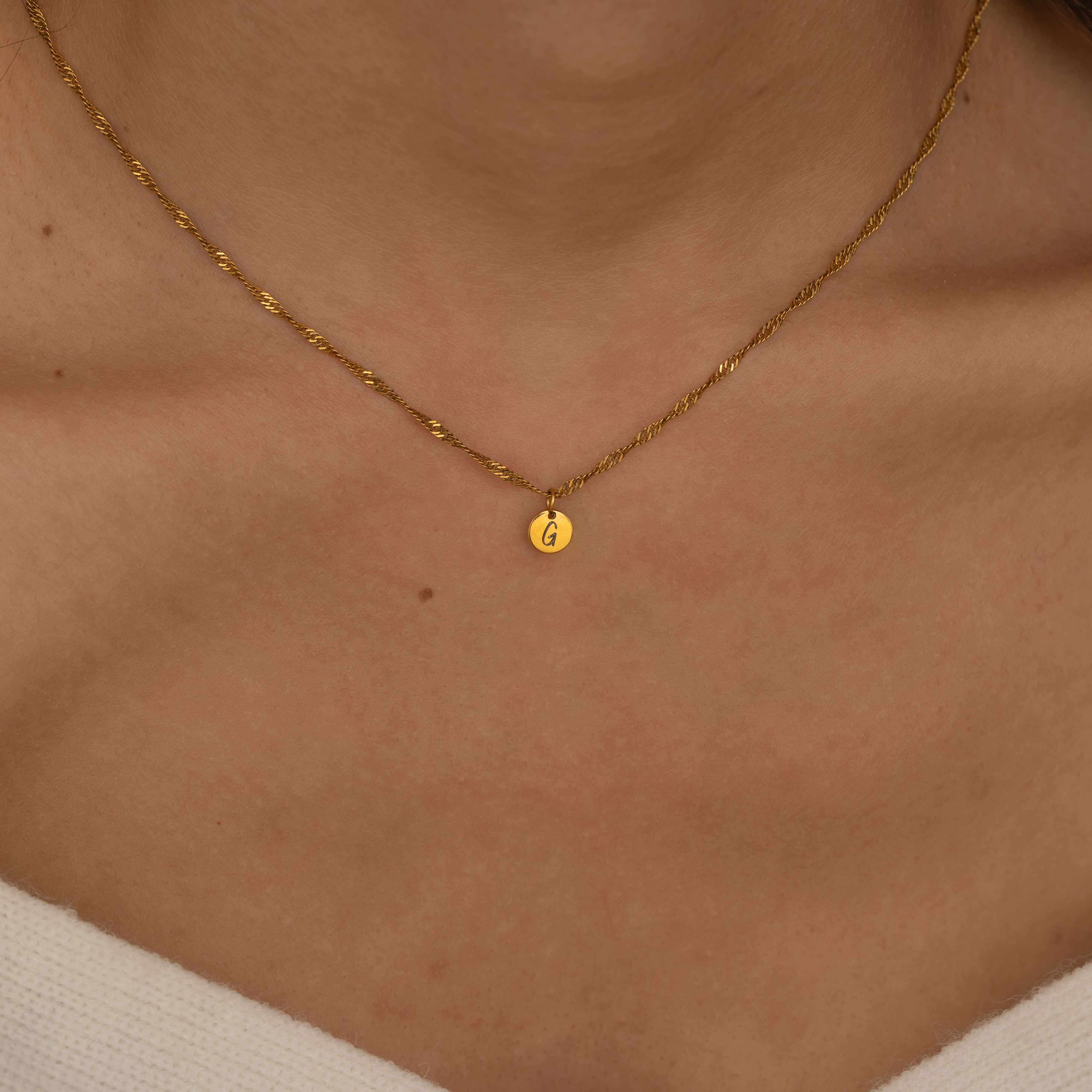 Three custom initial charm necklaces in gold, silver, and rose gold finishes, each with distinct chain styles and personalized round charms on a marble surface.