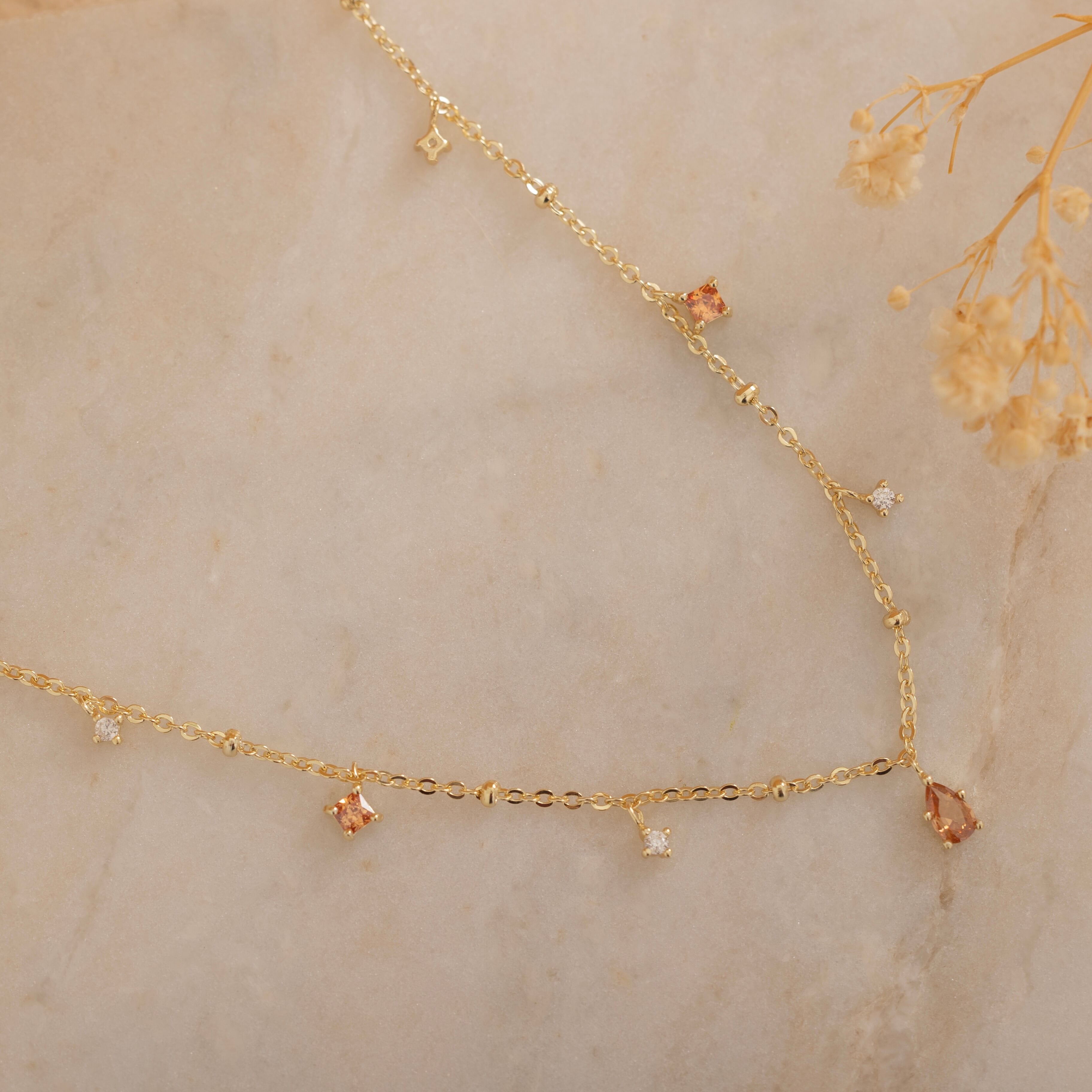 Dainty sterling silver and 14k gold plated necklace featuring four square champagne topaz-colored cubic zirconia stones, one centered teardrop-shaped champagne topaz stone, and four white cubic zirconia accents between the champagne topaz. 