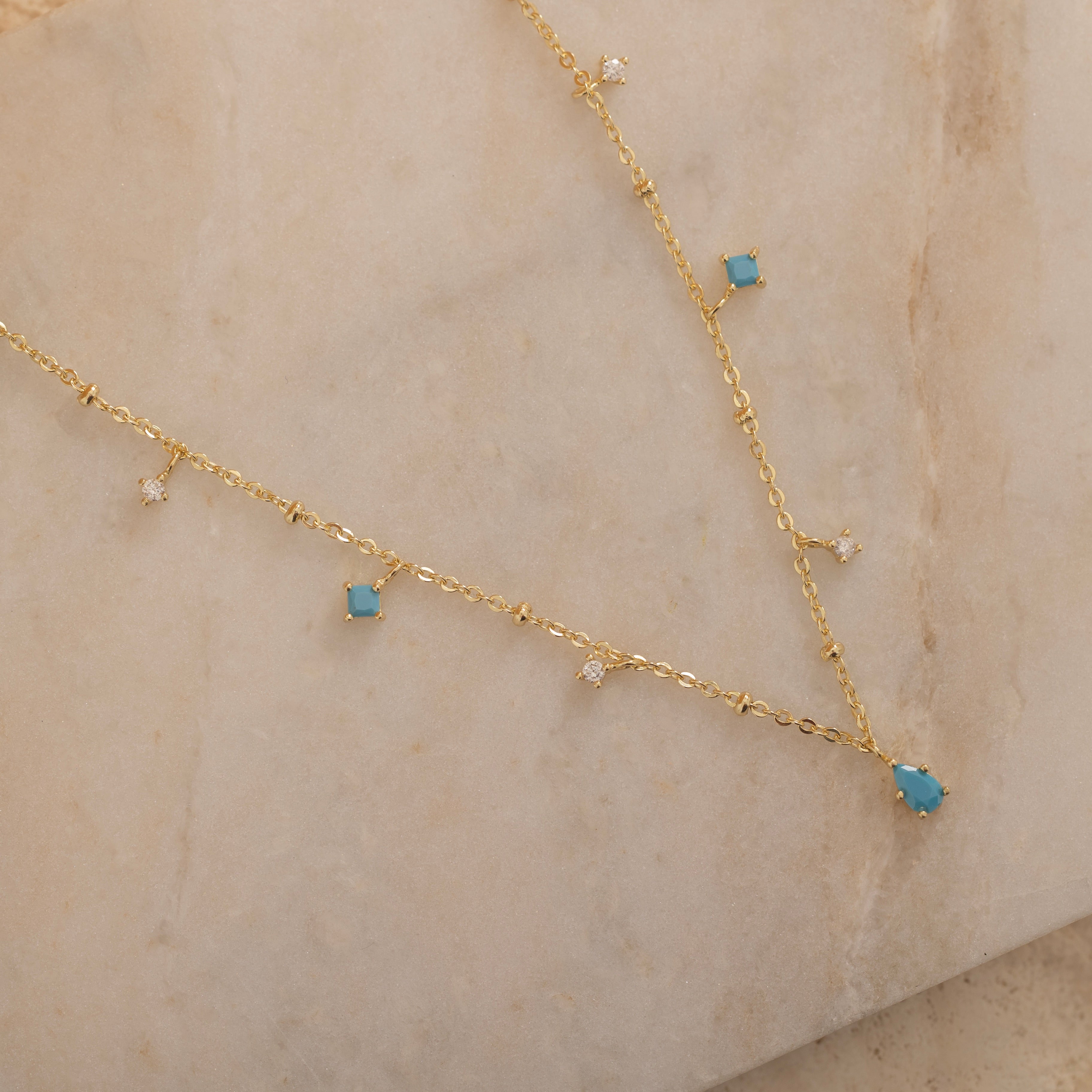 Dainty sterling silver and 14k gold plated necklace featuring four square turquoise birthstone stones, one centered teardrop-shaped turquoise stone, and four white cubic zirconia accents between the turquoise stones. Perfect for mother’s day and prom. 