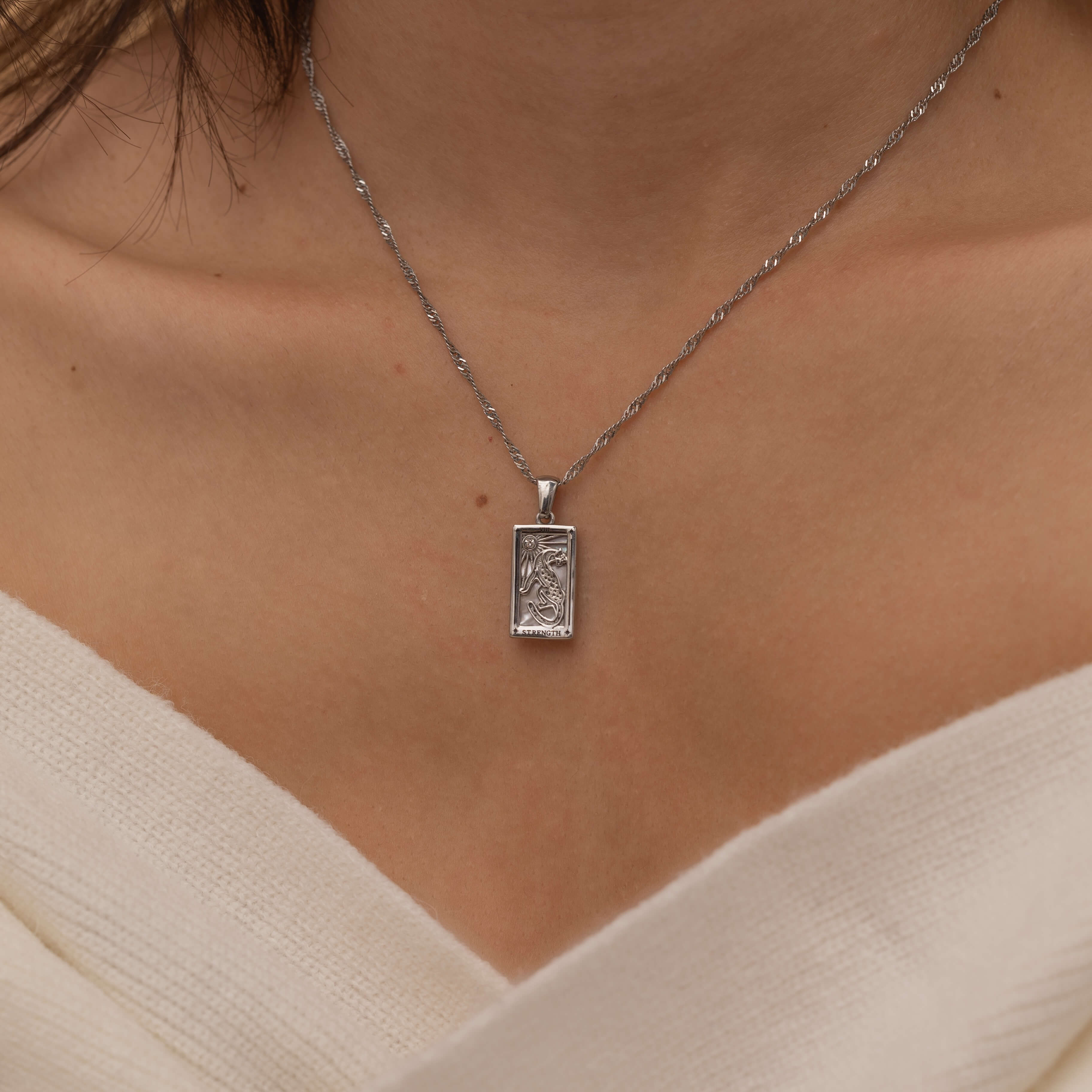 Gold and silver rectangular pendants with tiger engravings, featuring a sparkling cubic zirconia accent. They symbolize the strength tarot necklace. Available in both gold-plated and sterling silver chains.